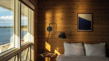 A room with a bed, a table with books, a lamp, and a painting on the wall.