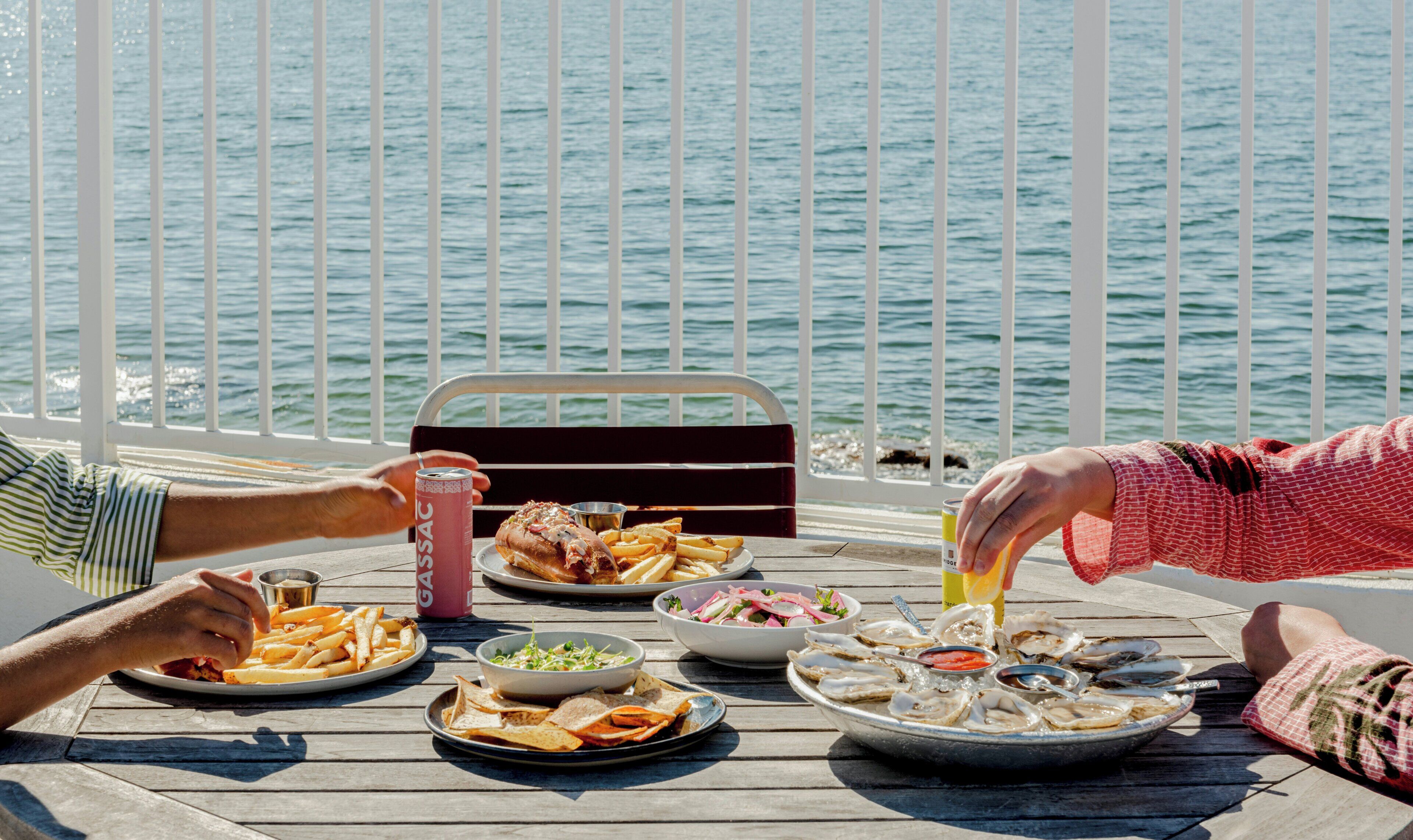 A dining table with various dishes, a drink, and a view of the water.