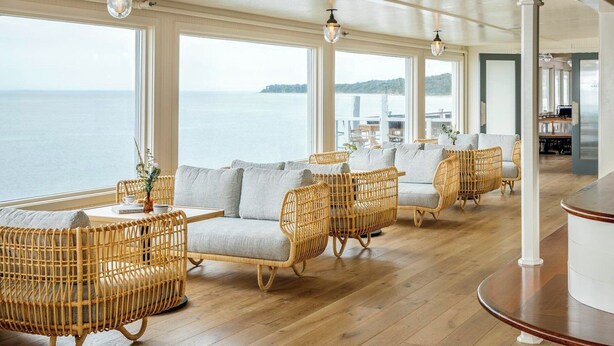 A spacious room with wicker furniture, large windows, and a view of the sea. - Sound View Greenport (Greenport)