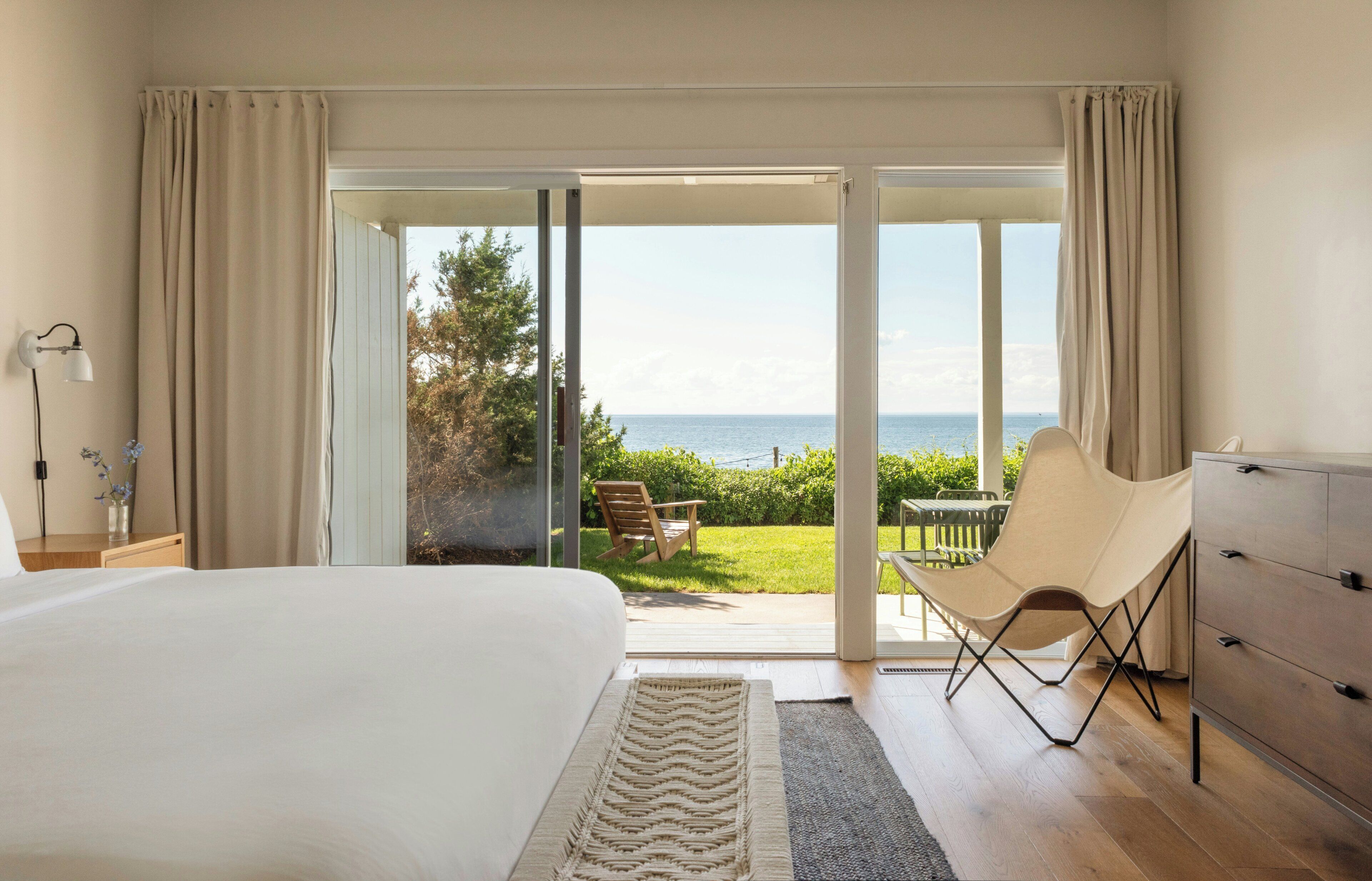 Une chambre avec un grand lit, une commode en bois, une chaise et une vue sur l’extérieur.