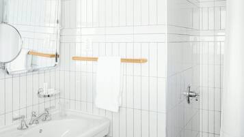 A modern bathroom with white tiles, a sink, a mirror, a towel rack, and a shower.