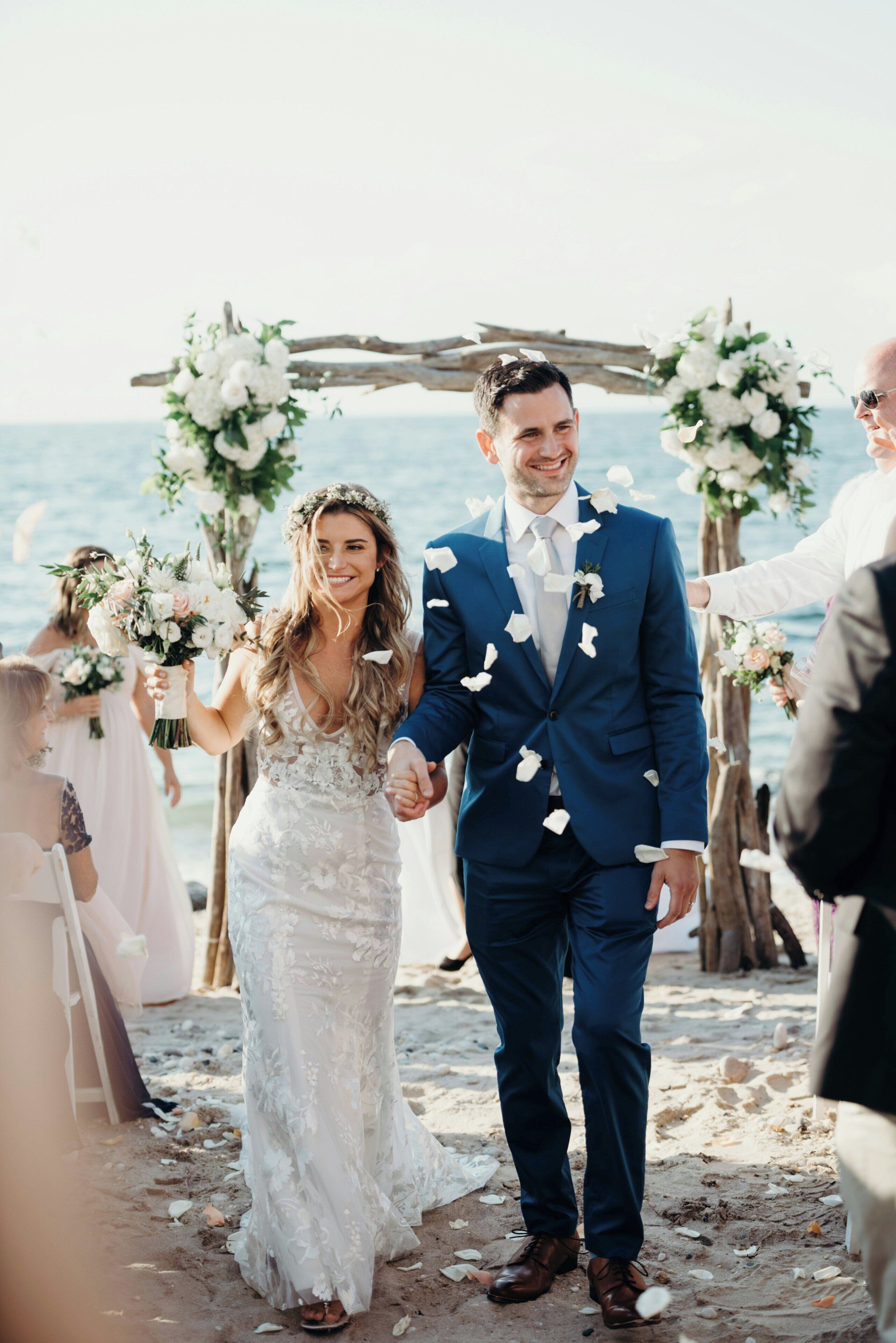 A wedding ceremony on a beach with a wooden arch and floral decorations.