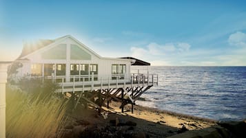 A white beachfront house with a balcony and a view of the ocean.