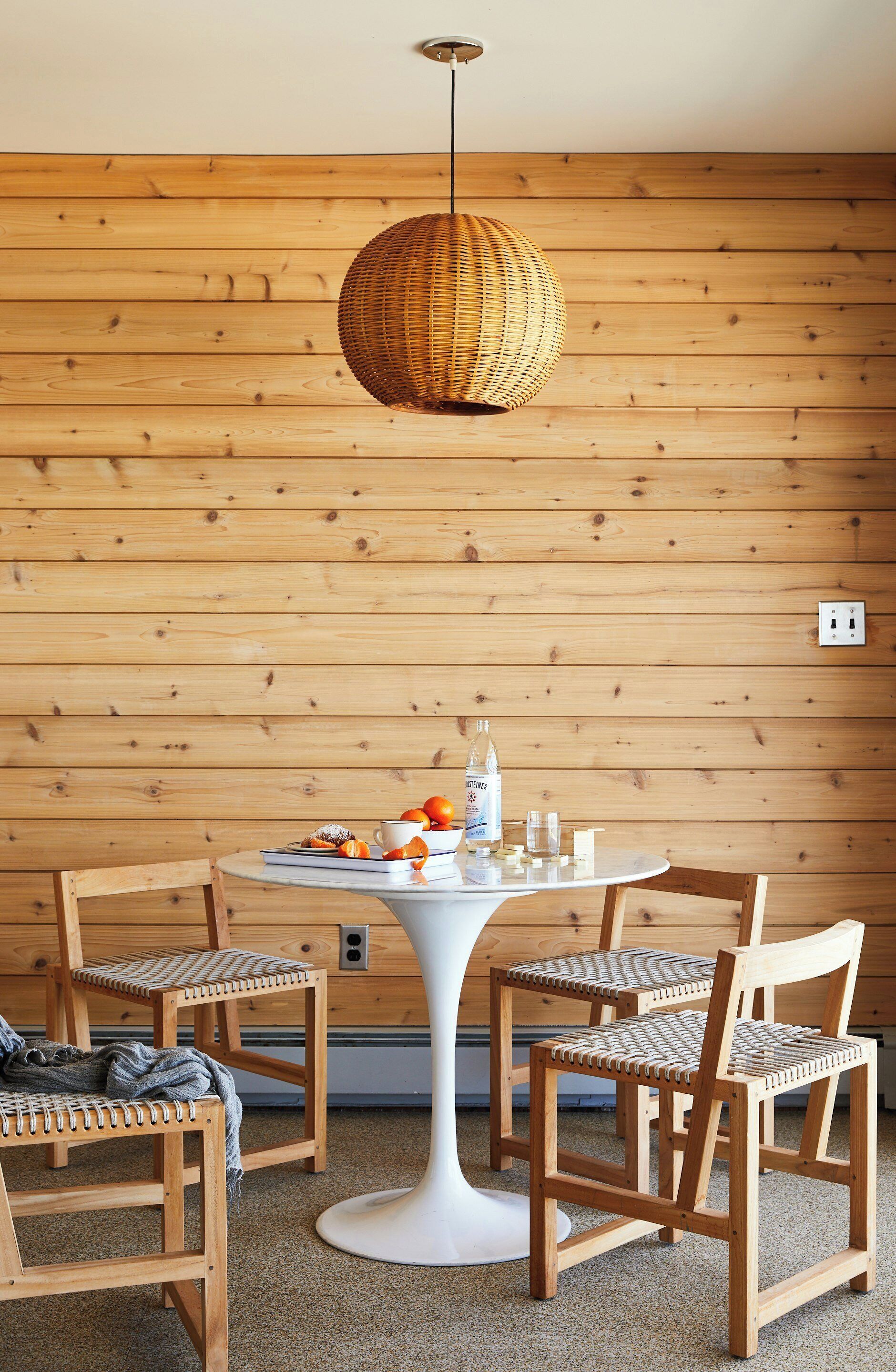 A wooden-paneled room with a round table, four chairs, a hanging light fixture, and a power outlet on the wall.