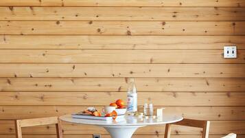 A wooden-paneled room with a round table, four chairs, a hanging light fixture, and a power outlet on the wall.