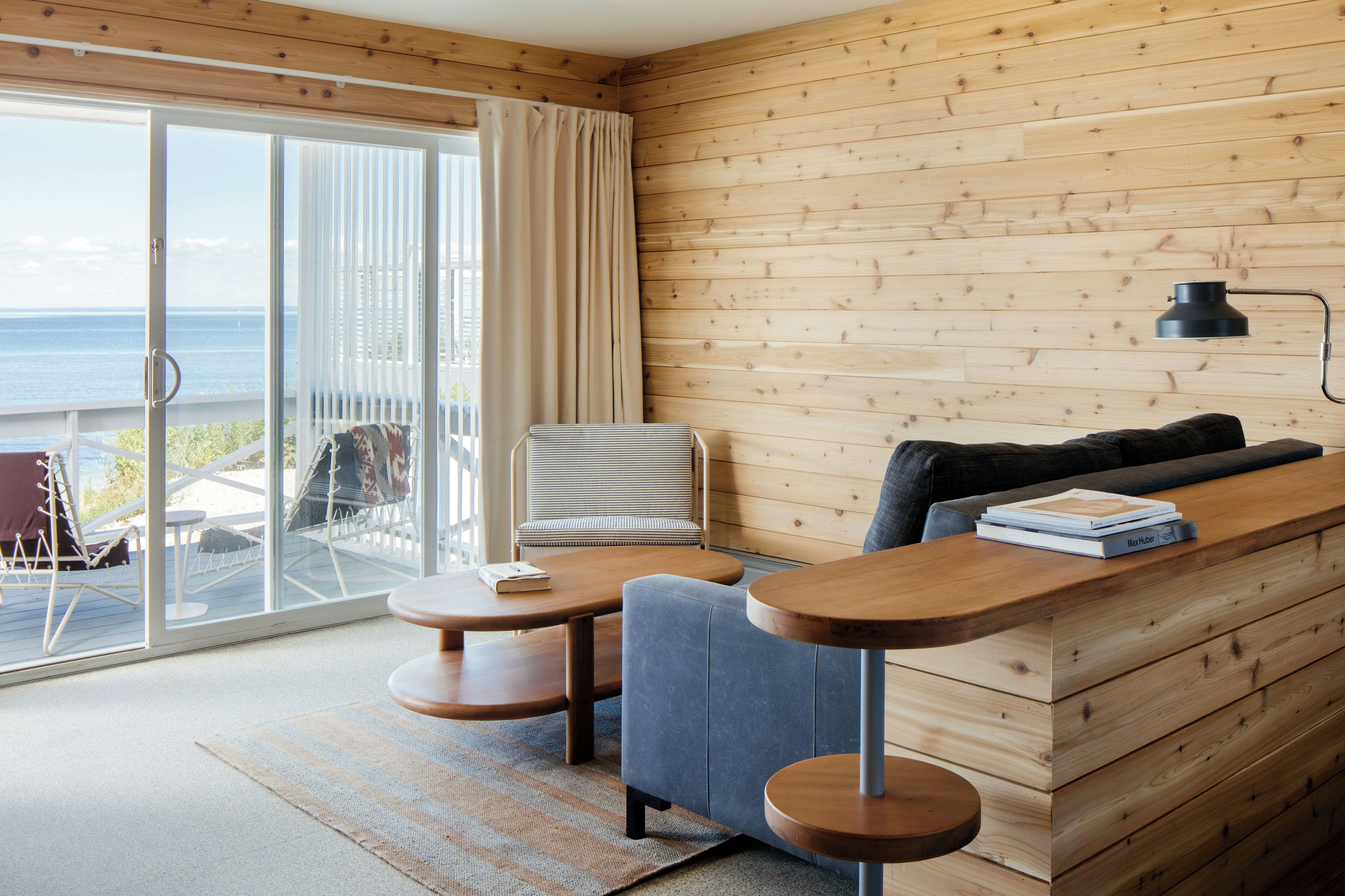Una sala de estar moderna con una pared de madera, un sofá, una mesa de comedor y vistas al mar a través de una puerta corredera.