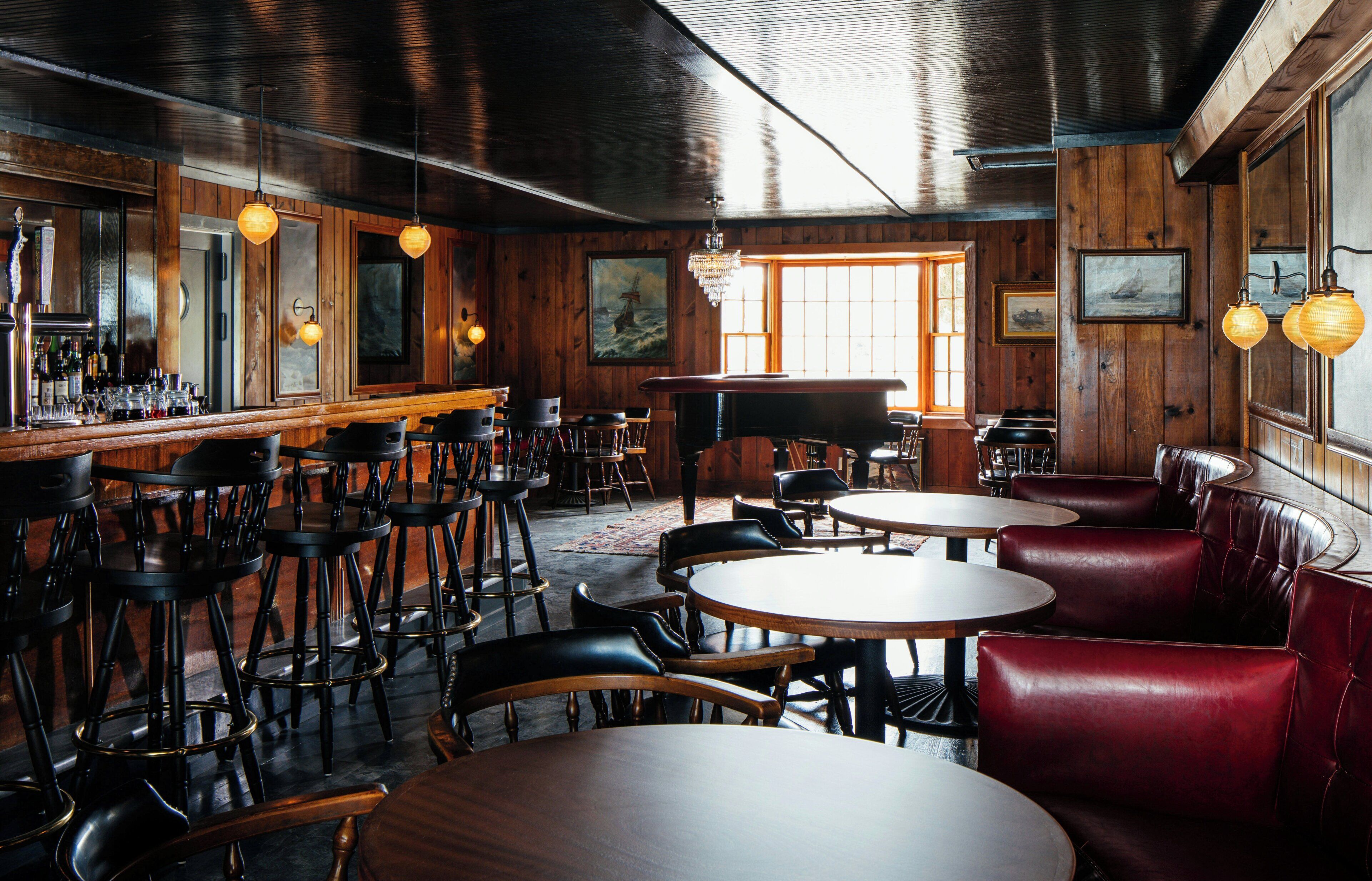 A bar area with wooden walls, multiple seating options including round tables and booths, and a piano.