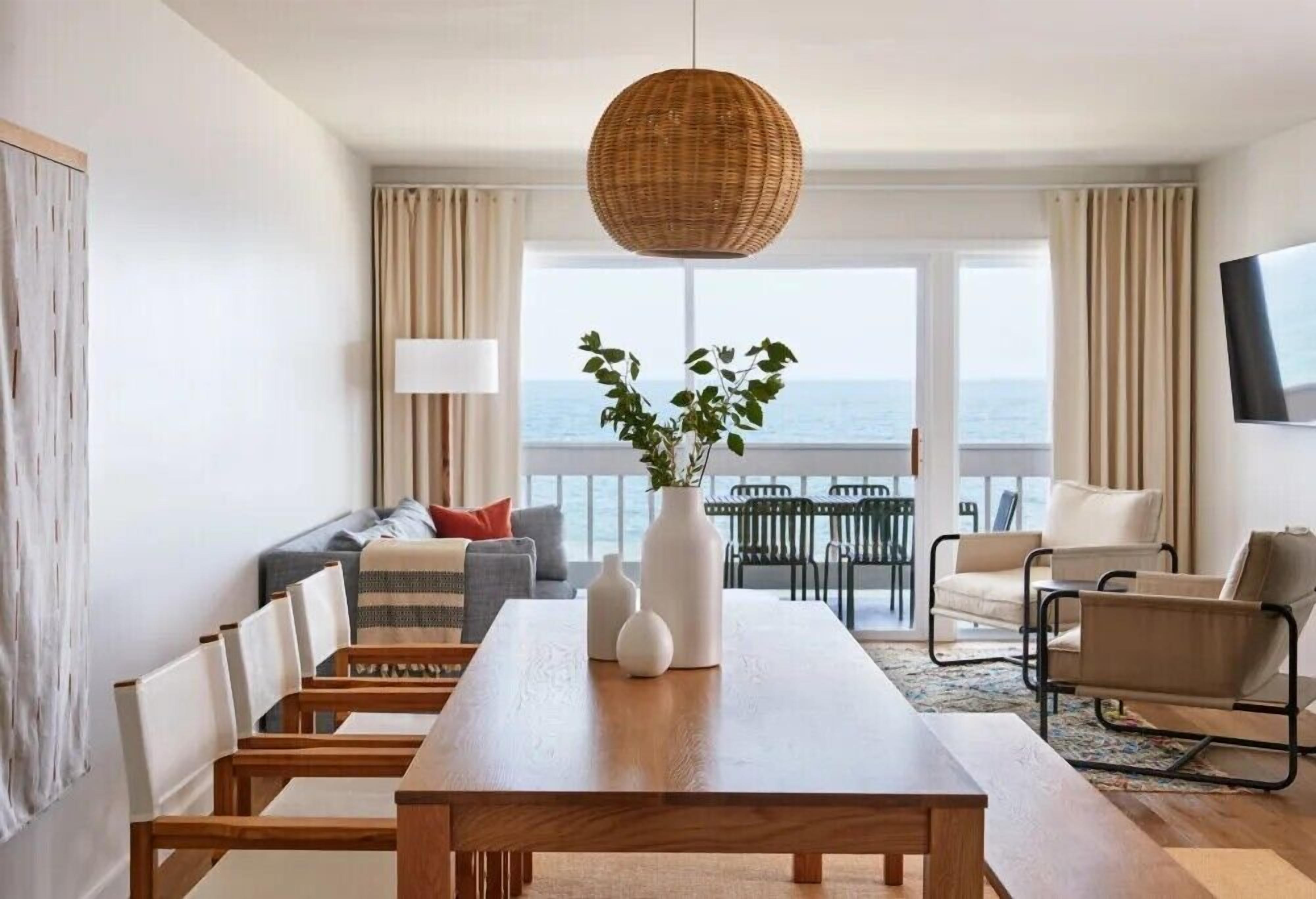 A modern living room with a dining table, sofas, and a view of the sea.