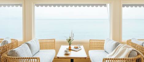 A room with wicker sofas, a small table with a vase, and a view of the sea.