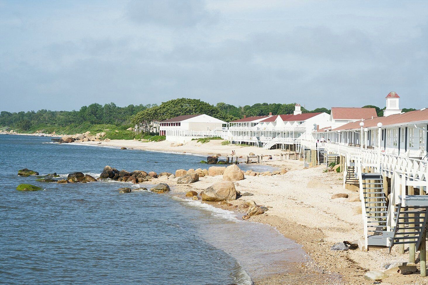 A coastal hotel with a beach view, a pier, and a lighthouse in the background.