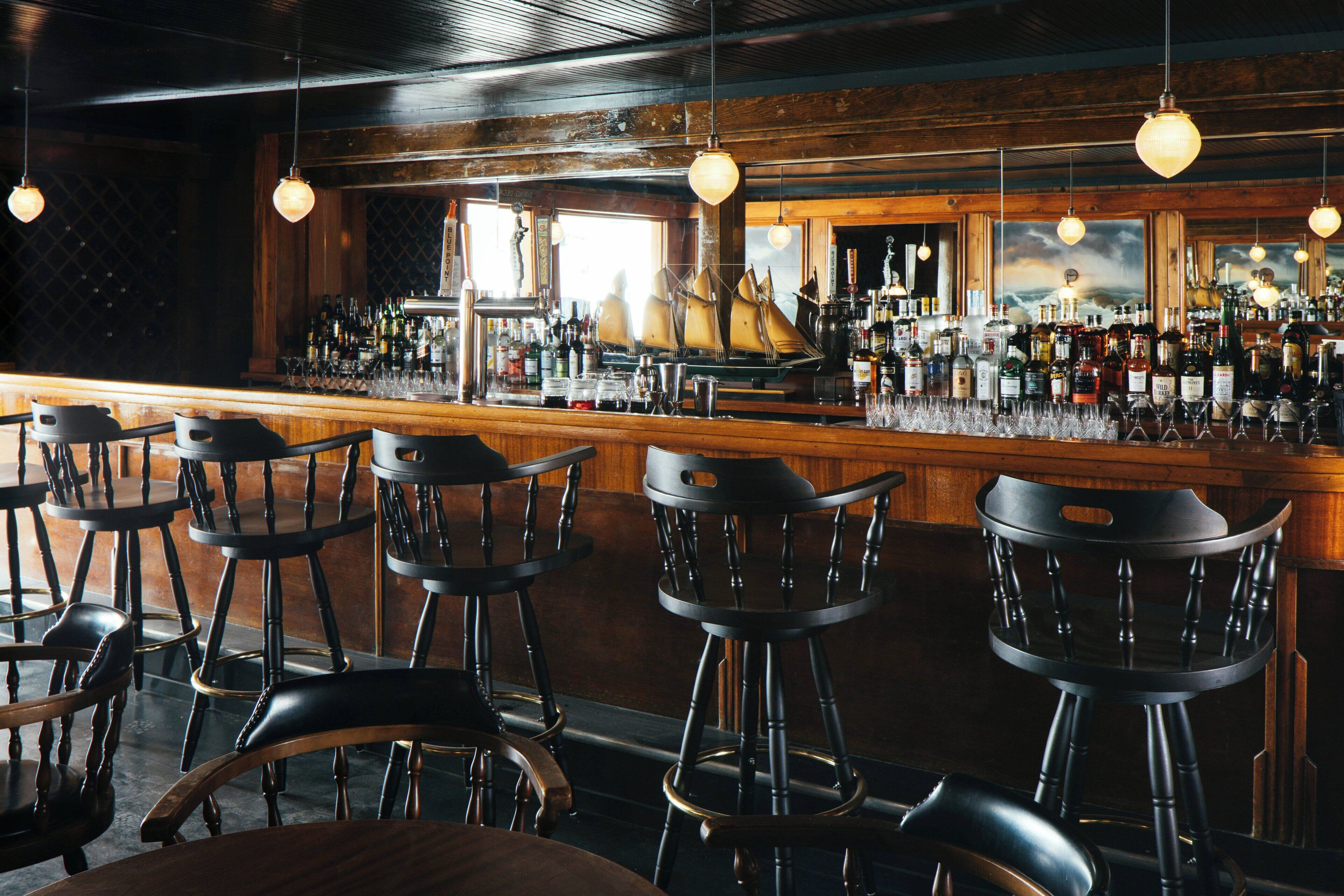 A bar area with wooden bar stools, a variety of bottles, and a large window with a view.