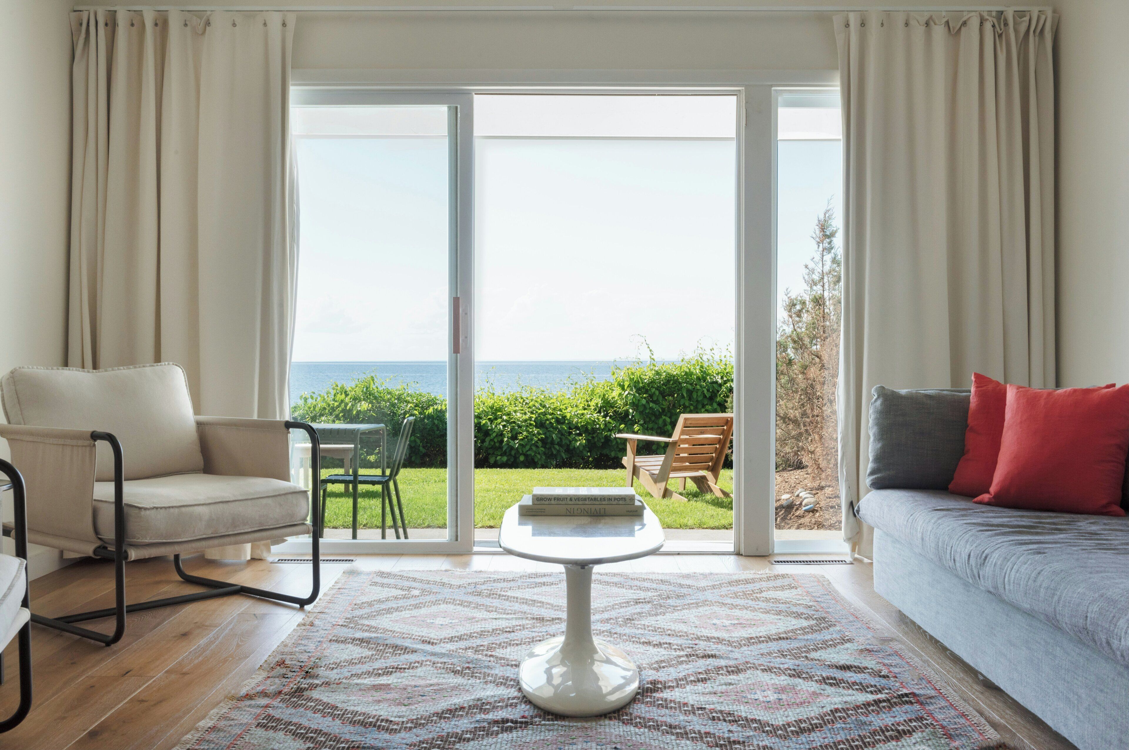 Un salon comprenant un canapé, un fauteuil, une table et une vue sur l’extérieur, visible à travers une porte vitrée.
