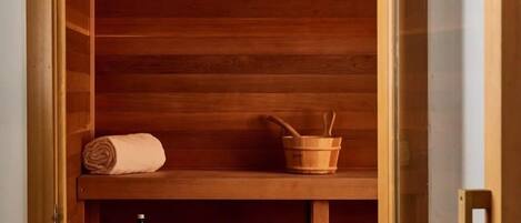 A wooden sauna with a bench, a towel, a bucket, and a bottle.