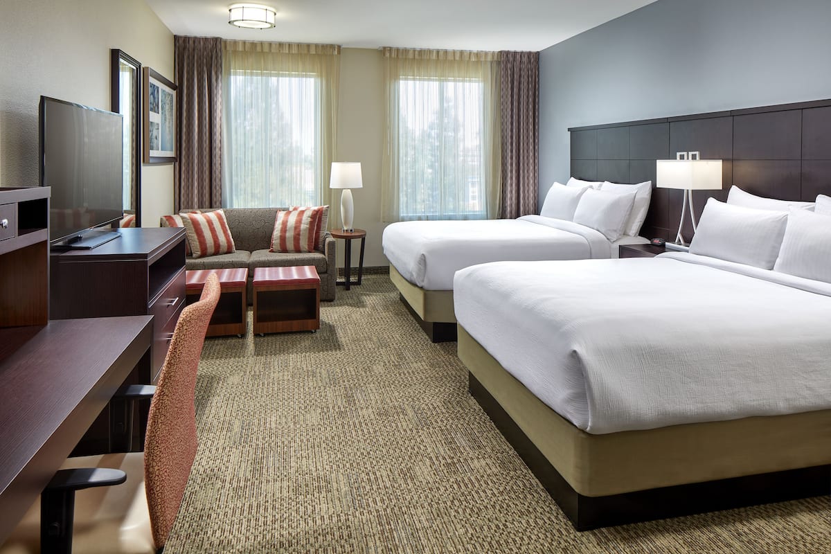 A hotel room with two beds, a desk, a TV, a sofa, and a carpeted floor.