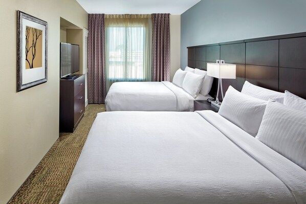 Habitación de hotel con dos camas, televisor, escritorio y ventana con cortinas.