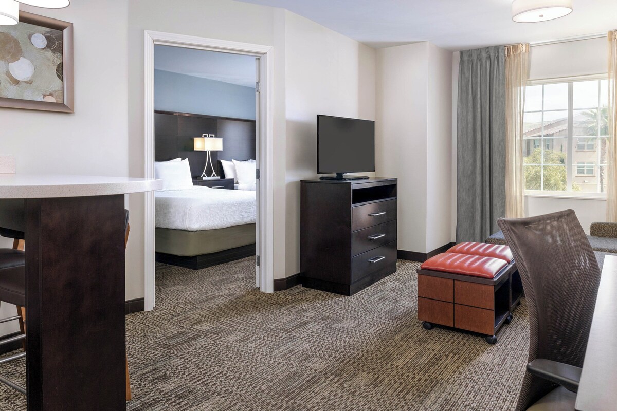 A hotel room with a bed, a desk, a television, a chair, and a window with curtains.