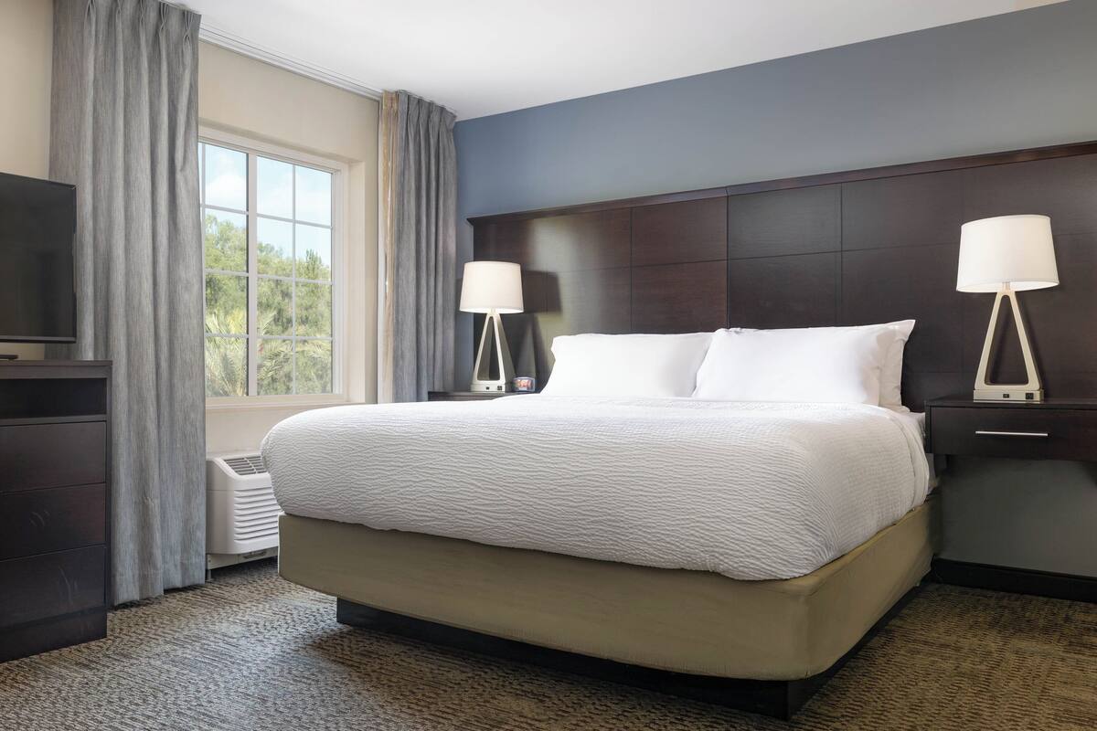 A hotel room with a large bed, two bedside lamps, a TV, and a window with curtains.