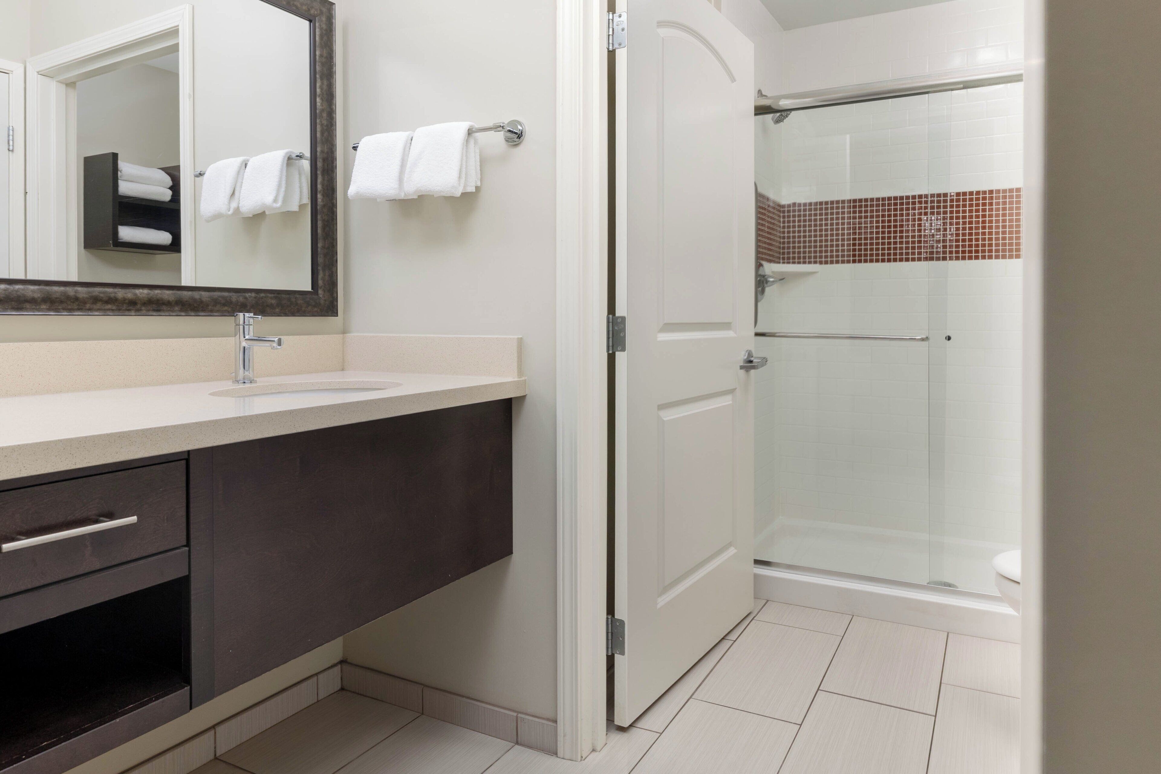 A modern bathroom with a vanity, a mirror, a shower enclosure, and a door leading to a tiled shower area.