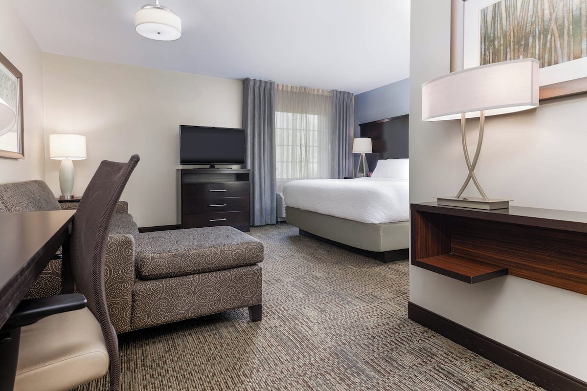 A hotel room with a bed, a desk with a chair, a television, a lamp, and a painting on the wall.