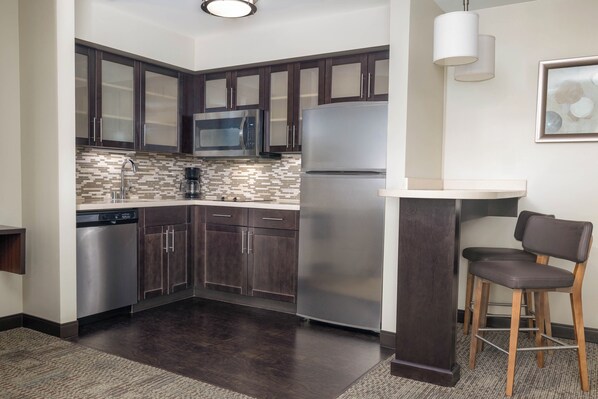 A modern kitchen with dark cabinets, stainless steel appliances, a tiled backsplash, and a bar area with stools.