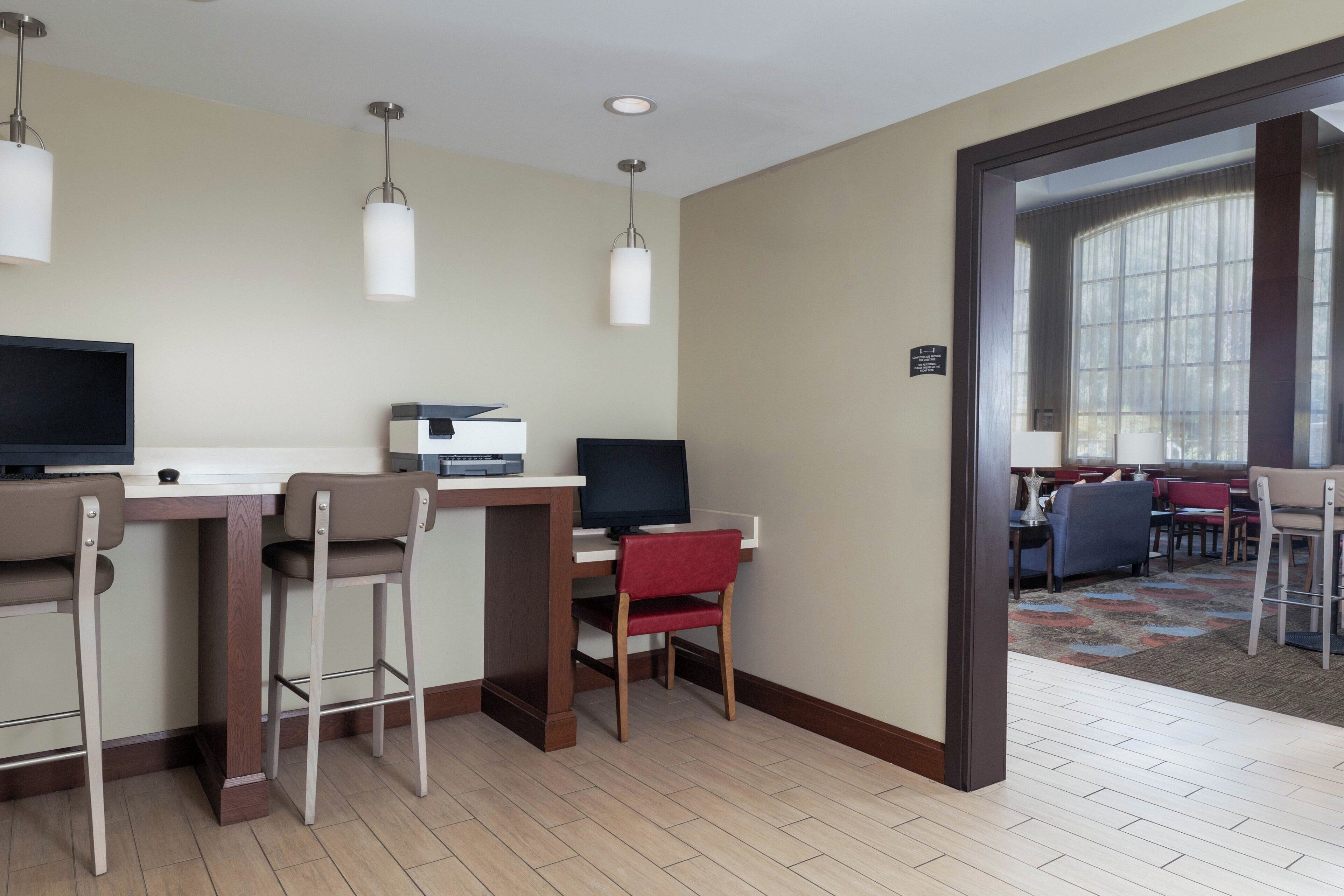 A hotel room with a desk, two chairs, a television, and a large window.