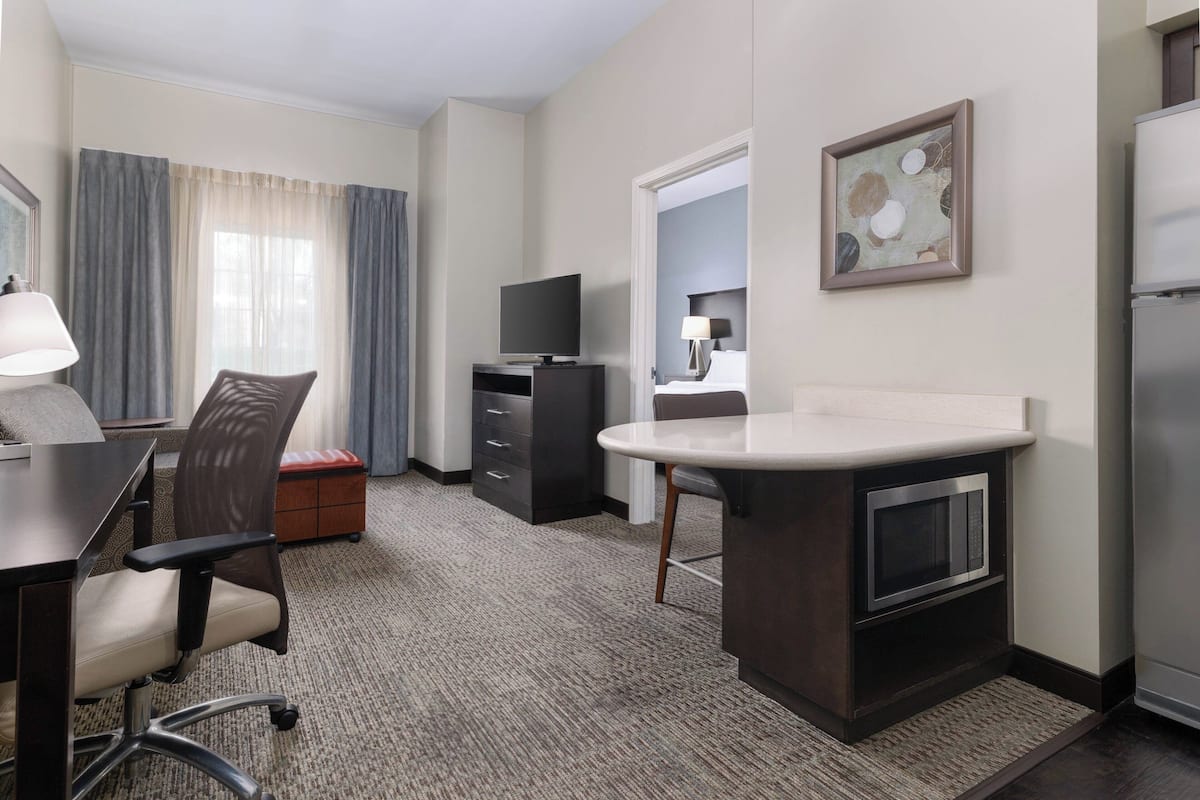 A hotel room with a desk, chair, television, minibar, and a large mirror.