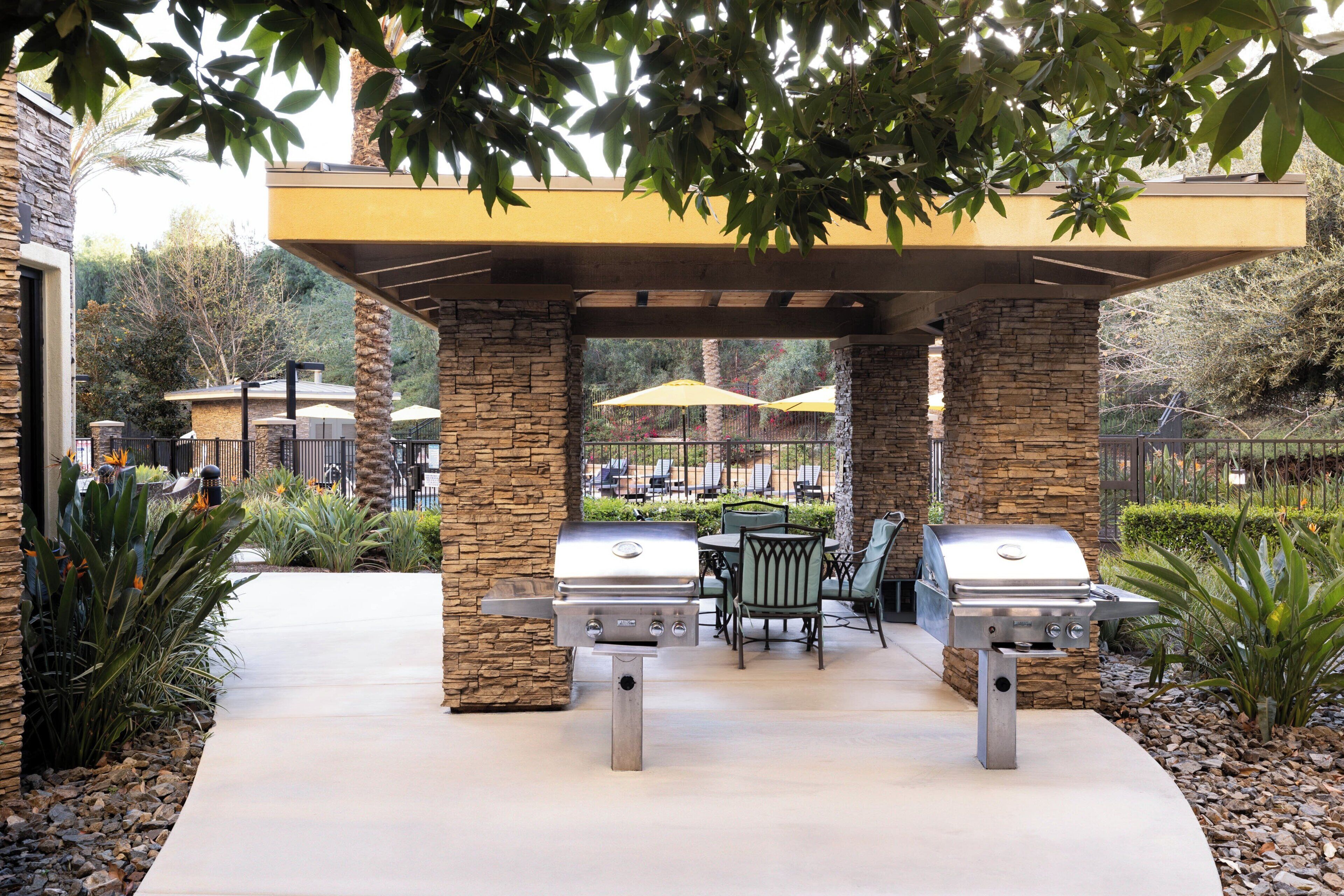 An outdoor patio with two barbecue grills, stone pillars, and a covered seating area.