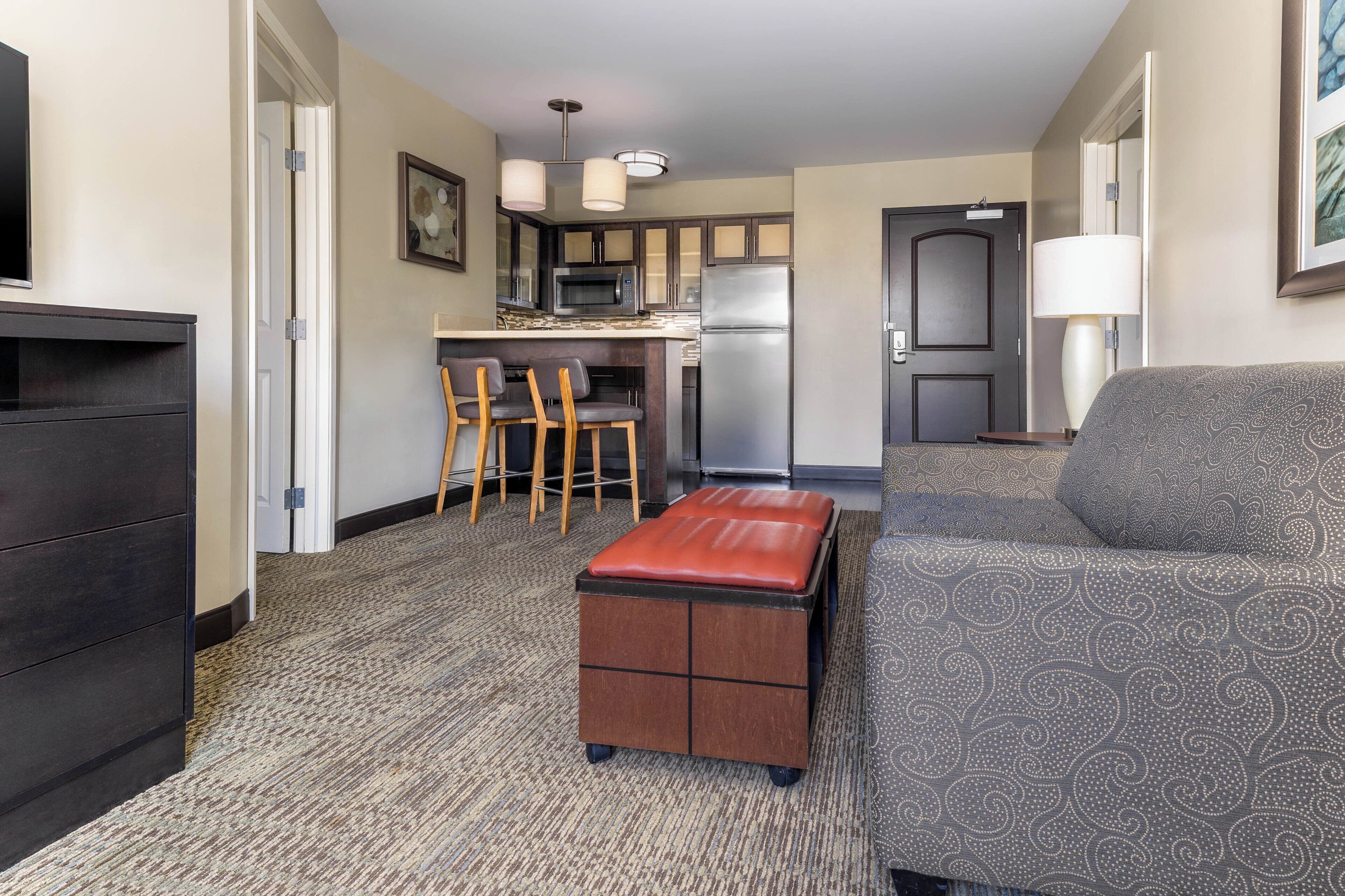 A compact living space with a kitchenette, a sofa, a small ottoman, and a TV.