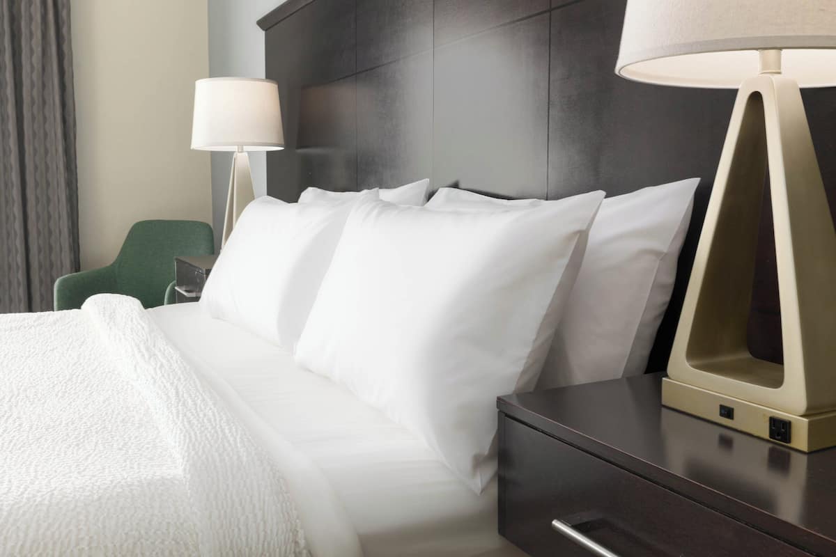 A hotel room with a bed, a nightstand, a lamp, and a green chair.