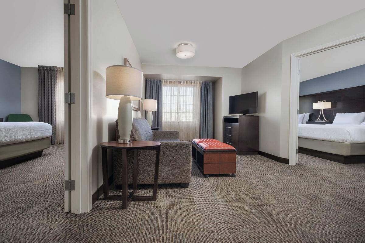 A hotel room with a bed, a desk with a lamp, a television, a dresser, and a window with curtains.