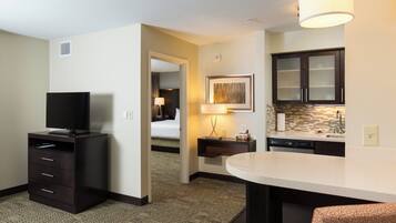 Habitación de hotel con televisión, escritorio con lámpara, cama y kitchenette.
