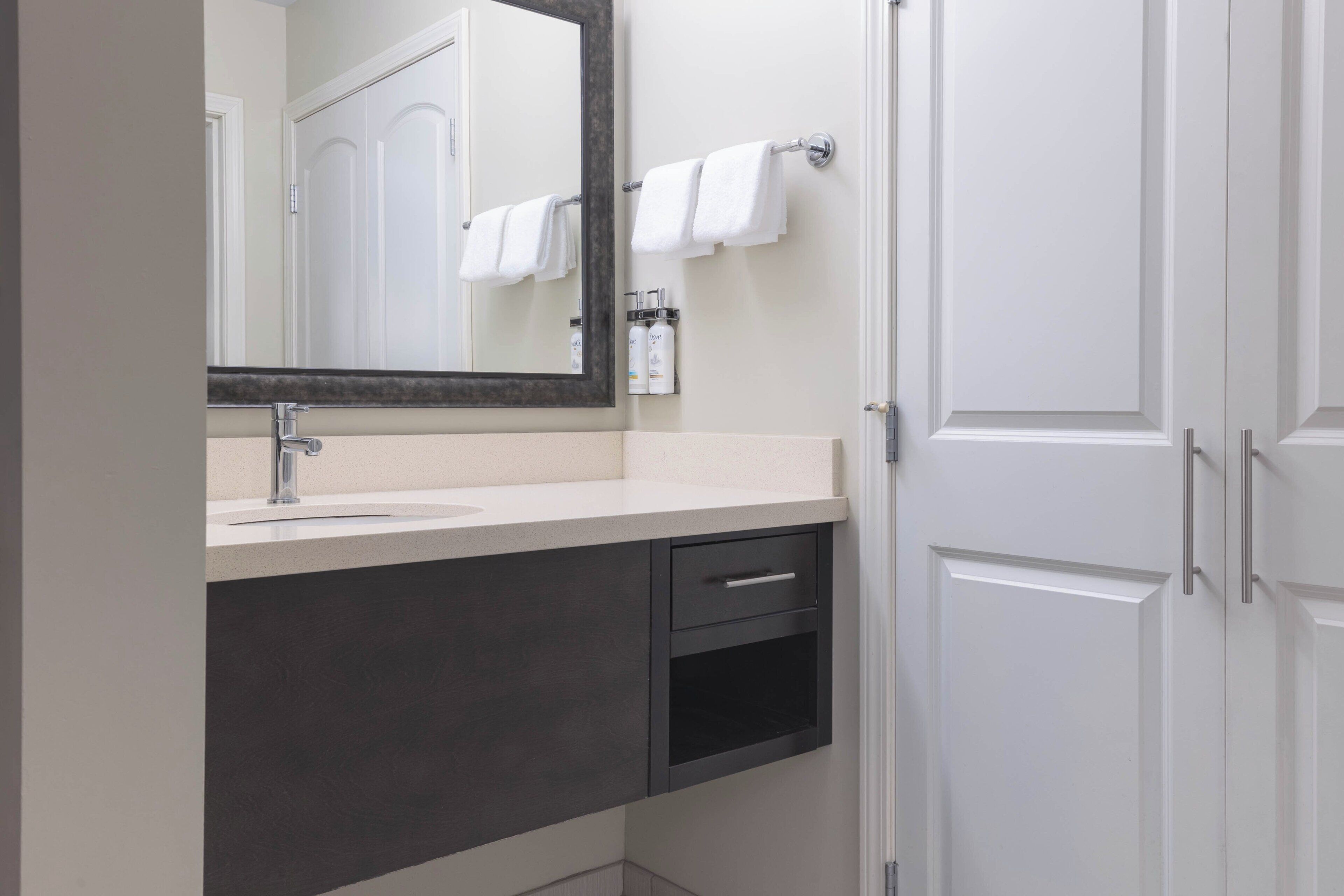 A modern bathroom with a sink, mirror, towel rack, and cabinets.