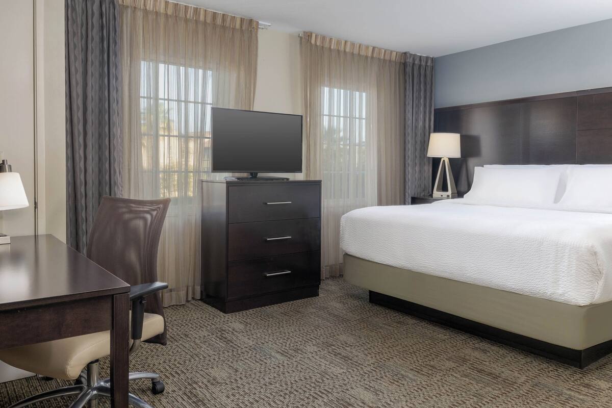 A hotel room with a bed, a desk, a chair, a TV, and a lamp.