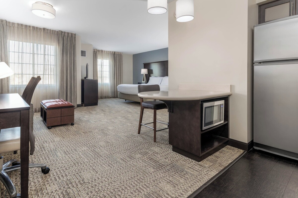A hotel room with a kitchenette, a bed, a desk, and a chair.