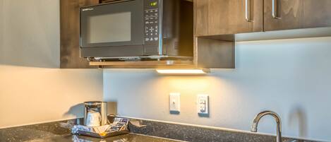 A kitchen with a microwave, a sink, and wooden cabinets.