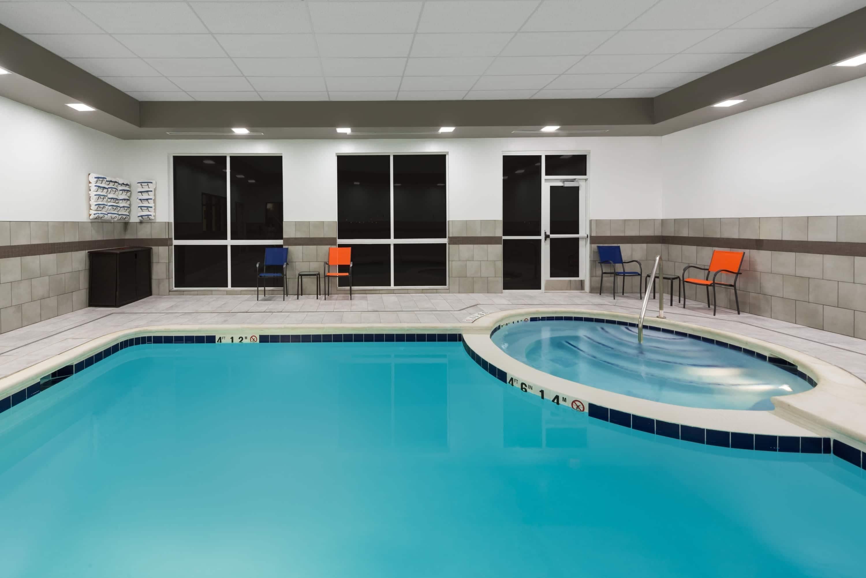 Une piscine dont le bord est recouvert de carreaux, quelques chaises et une porte donnant sur une autre pièce.