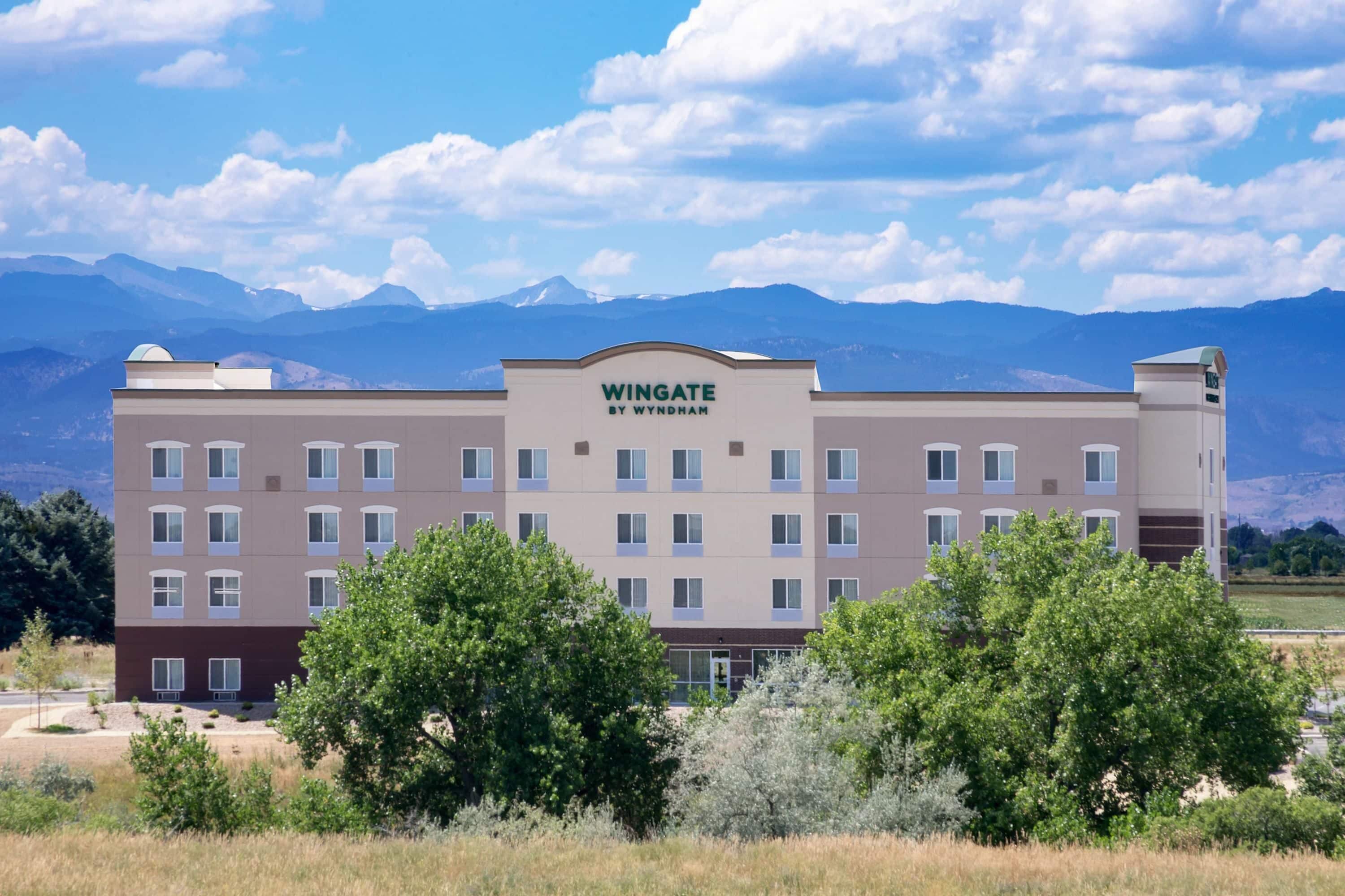 A multi-story hotel with a flat roof, a sign reading 'Wingate by Wyndham,' and a mountainous backdrop.