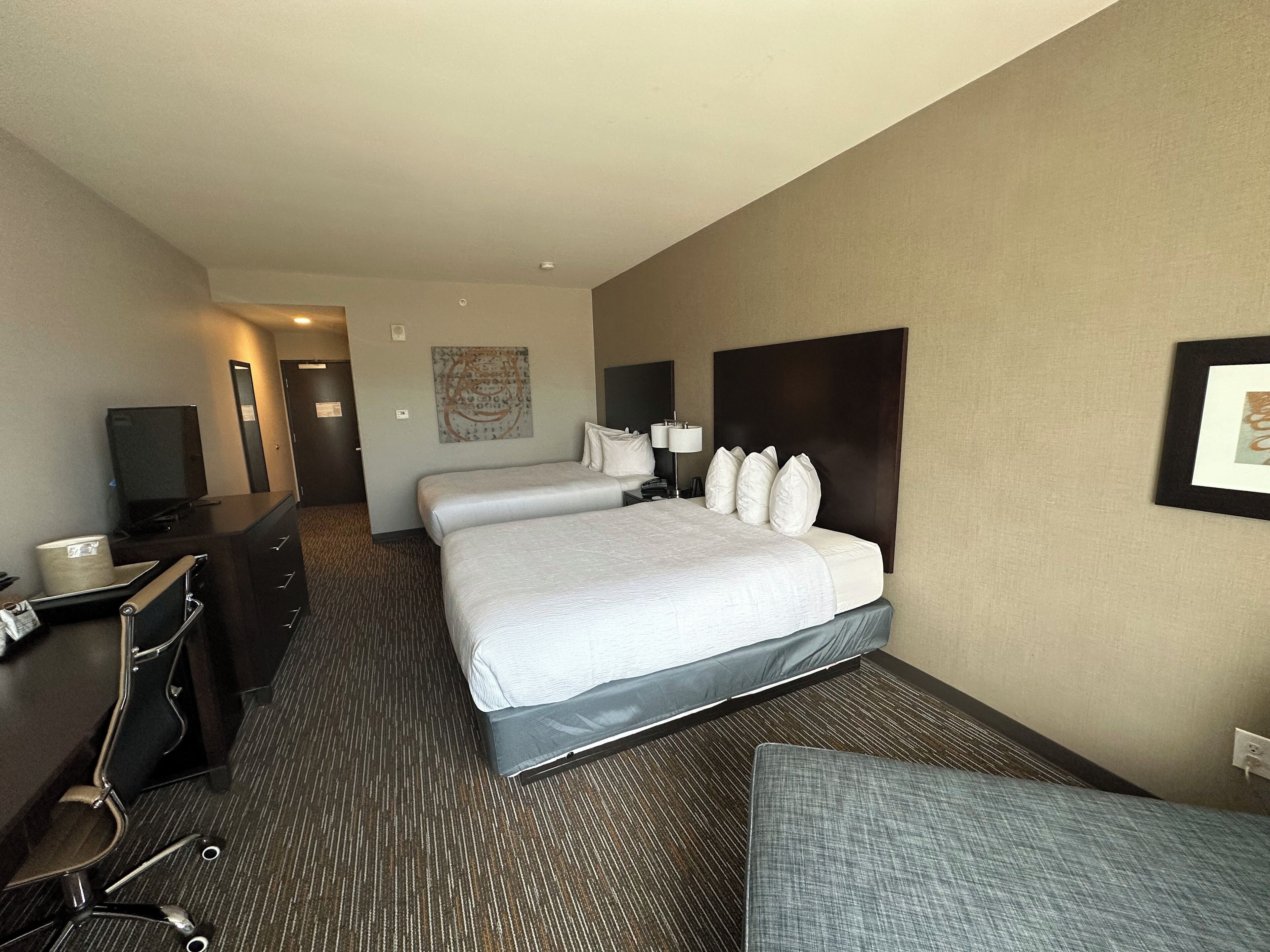 A hotel room with a large bed, a desk with a computer, a chair, and a television.
