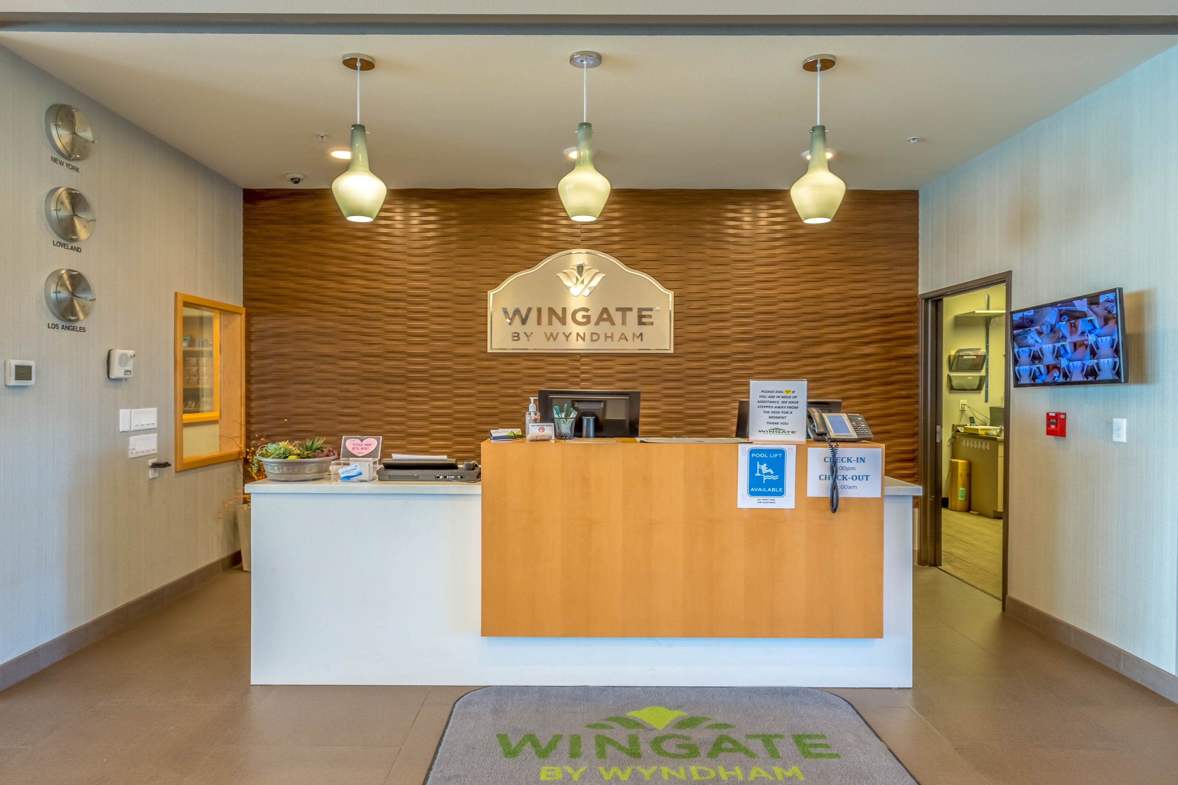 A reception desk with a wooden finish, a sign reading "Wingate by Wyndham", and a check-in/check-out counter.