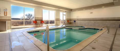 Une piscine intérieure avec des parois en verre transparent, un sol carrelé et une vue sur l’extérieur.