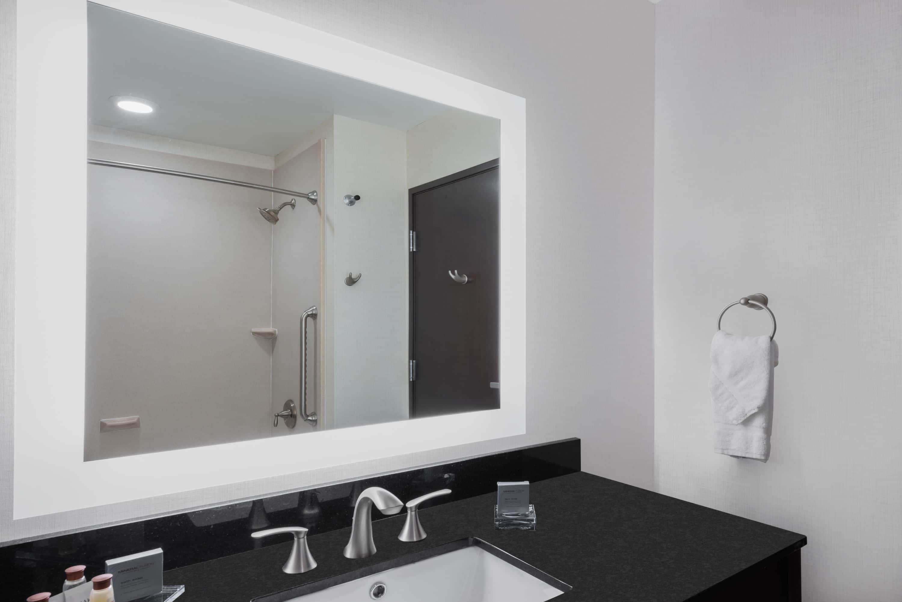 A modern bathroom with a large mirror, a black countertop, a white sink, and a towel rack.