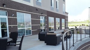 A covered outdoor patio with wicker furniture, a glass door entrance, and a view of a landscaped area. - Wingate by Wyndham Loveland (Loveland)
