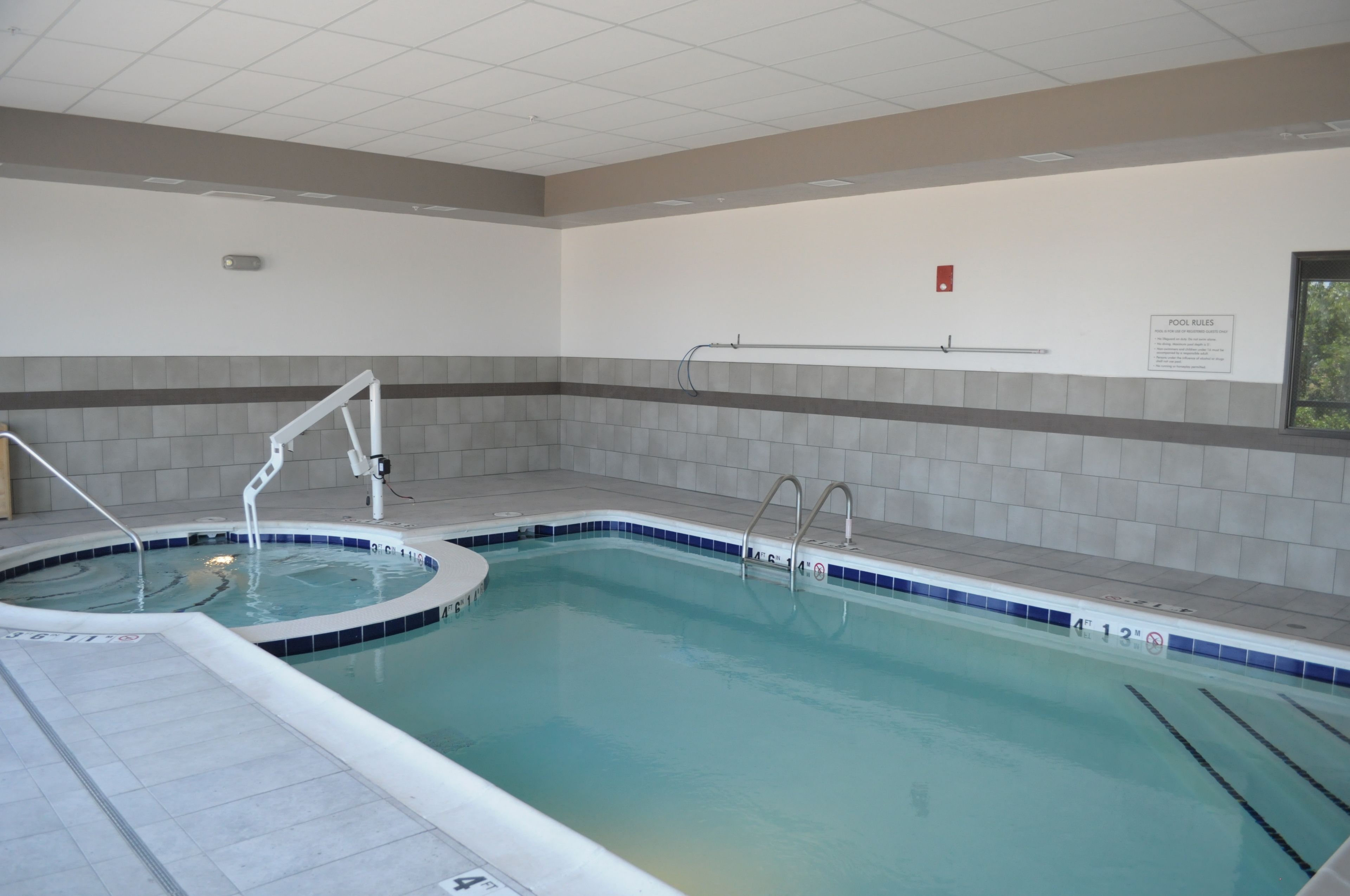 An indoor swimming pool with clear water, a diving board, and a 'POOL RULES' sign on the wall.