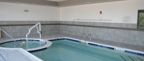 An indoor swimming pool with clear water, a diving board, and a 'POOL RULES' sign on the wall.