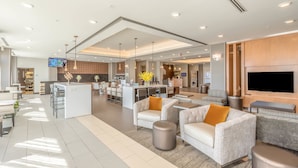A spacious hotel lobby with a central island, seating areas, a TV, and a modern kitchen in the background. - Wingate by Wyndham Loveland (Loveland)