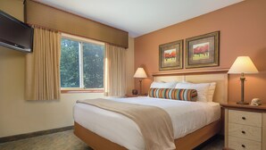 A hotel room with a large bed, two bedside lamps, a TV, and two framed paintings on the wall.