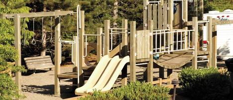 Un parque infantil con tobogán, estructuras para escalar y un banco.