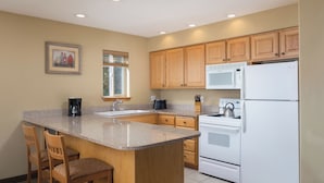 A kitchen with a granite countertop, wooden cabinets, a stainless steel range, a white refrigerator, and a window with blinds.