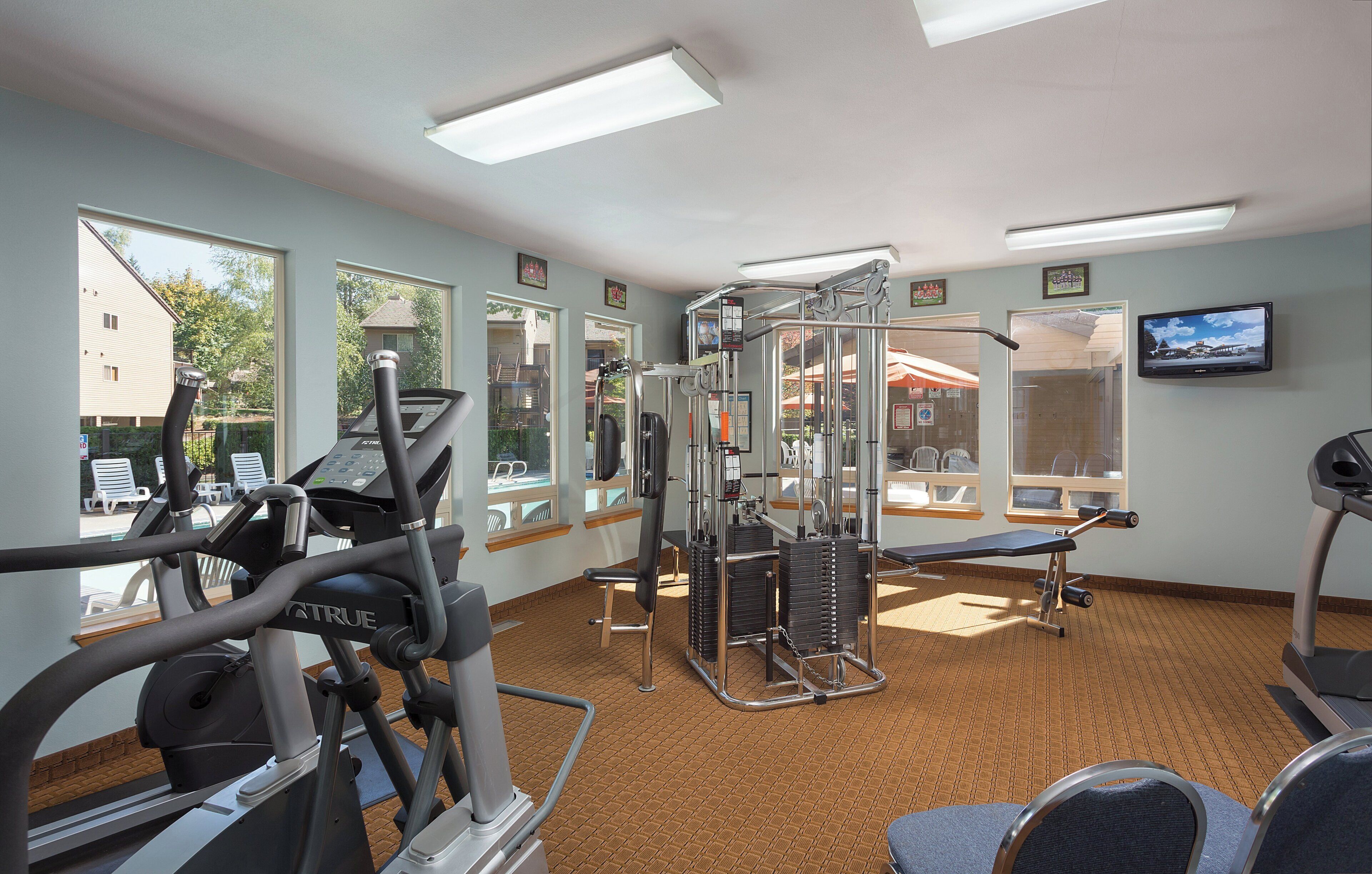 A gym with exercise equipment, a television, and large windows.