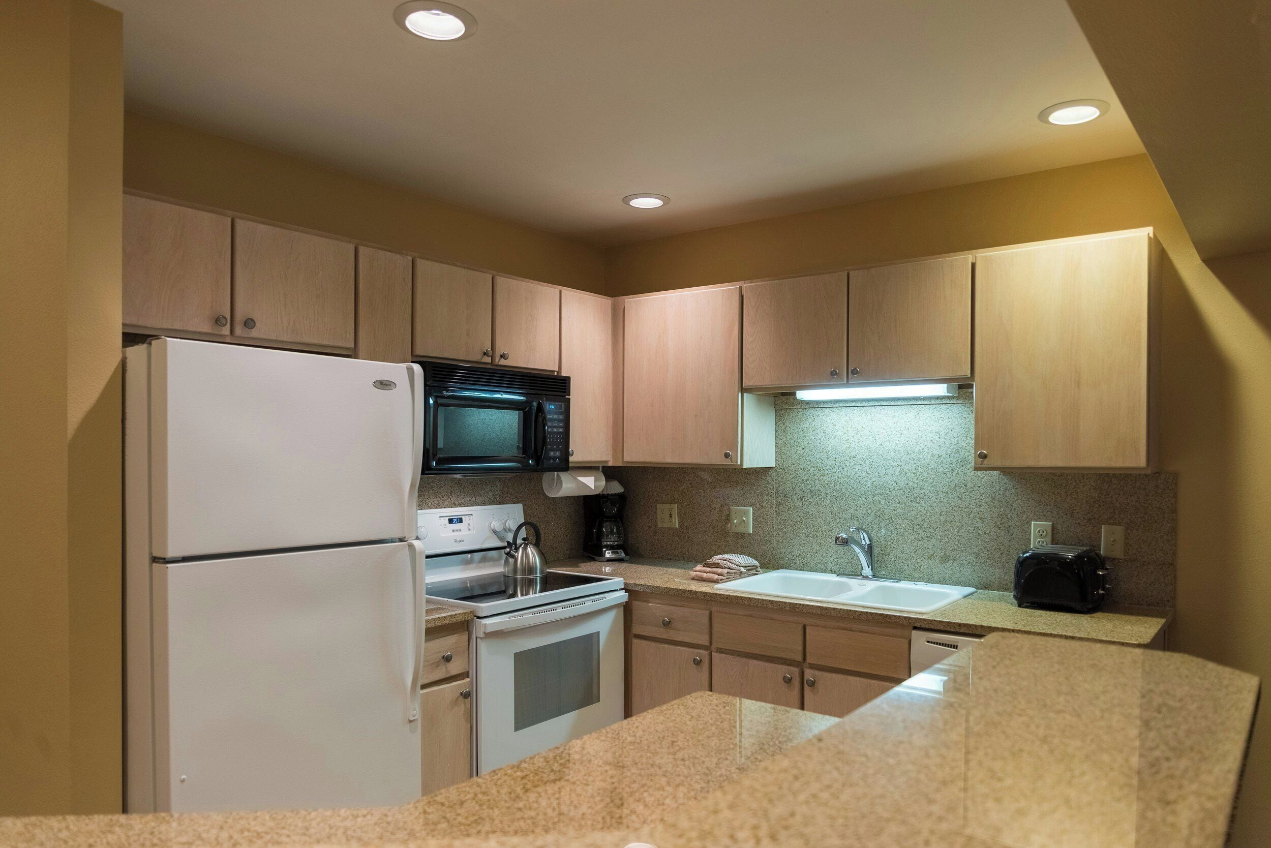 A compact kitchen with a refrigerator, microwave, stove, and sink.